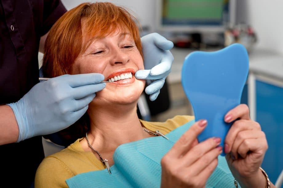 woman in dental chair holding mirror and looking at teeth