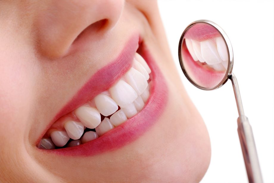 close up of young woman's smile and dental mirror