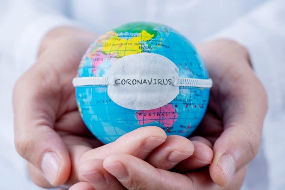 hands holding tiny globe that has mask with coronavirus written on it