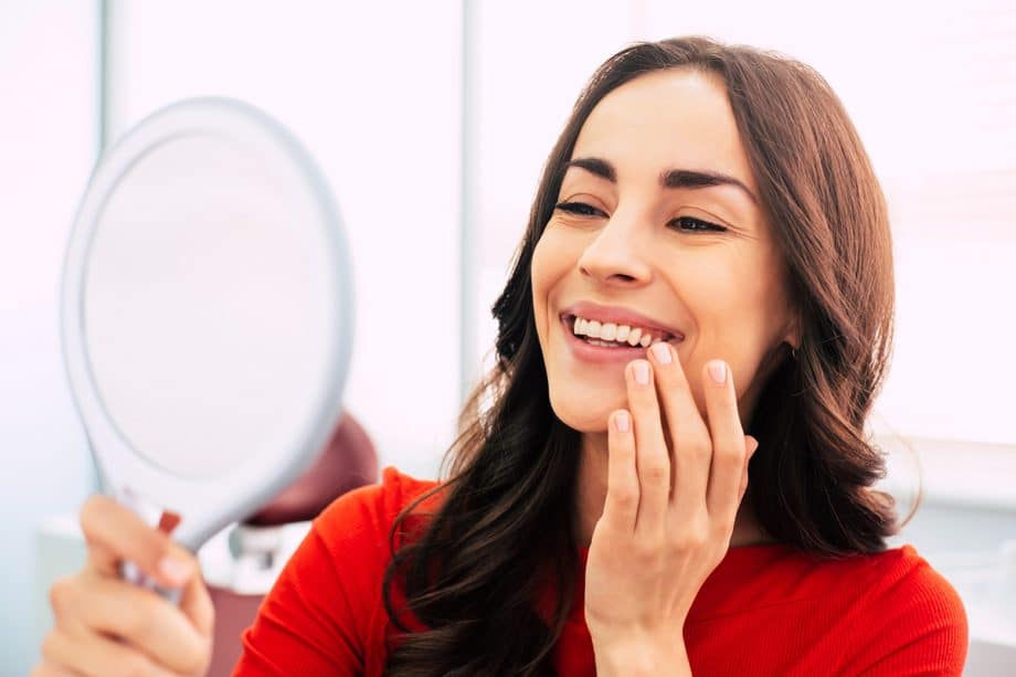 woman in red shirt looking in hand-held mirror and smiling